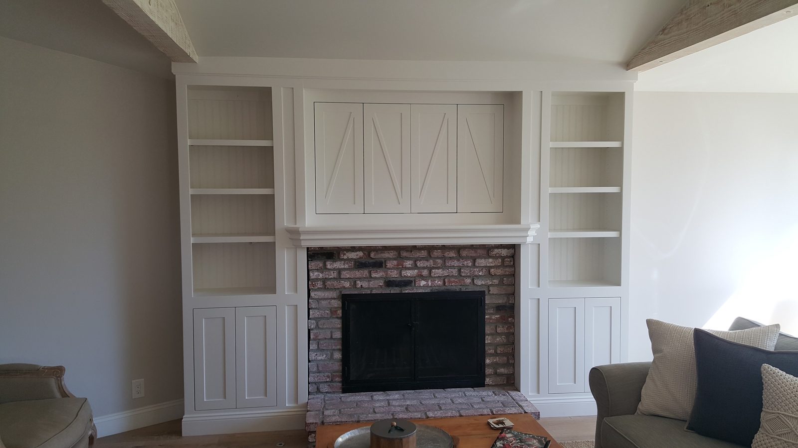 The same fireplace wall with the built-in shelves, cabinets and X-braced doors finished in a smooth white, the brick left as it was.